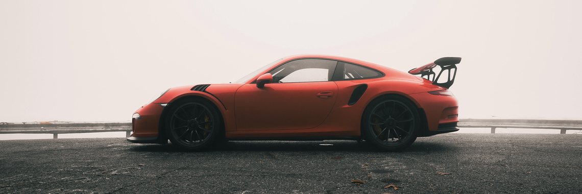 A 991.1 GT3 RS in Lava Orange, photographed in profile on a fog-covered mountain road.